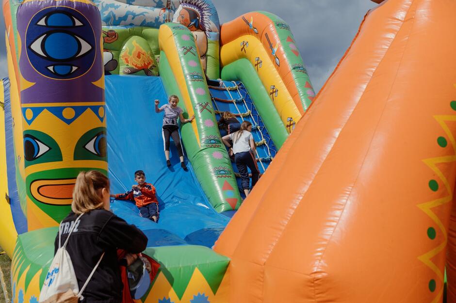Dzieci bawią się na kolorowej, dmuchanej zjeżdżalni, pod czujnym okiem opiekunów