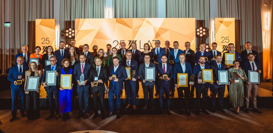 Zdjęcie przedstawia laureatów Pomorskiej Nagrody Gryf Gospodarczy 2024 podczas gali jubileuszowej z okazji 25-lecia wydarzenia. Uhonorowani przedstawiciele firm i instytucji pozują z dyplomami i statuetkami na tle sceny z okolicznościową grafiką.