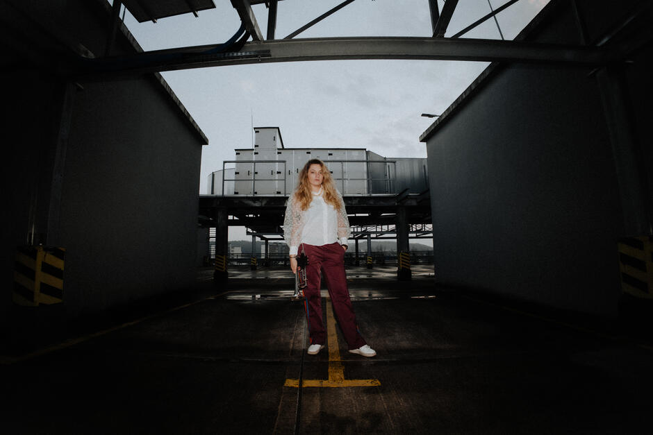 Na zdjęciu kobieta z włosami za ramiona, w tle budynki.