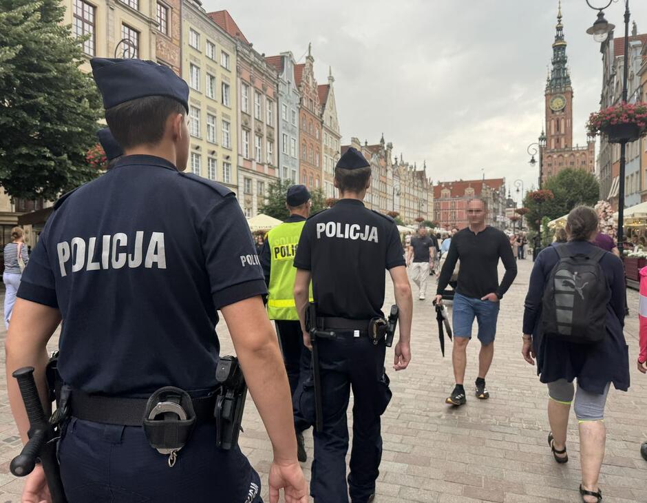 na zdjęciu trzech policjantów w mundurach patroluje ulicę gdańska, są odwrócenie tyłem do fotografującego