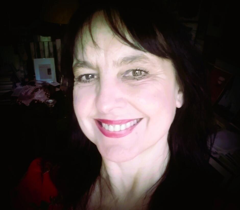 Na zdjęciu twarz uśmiechniętej kobiety z czarnymi włosami za uszy.