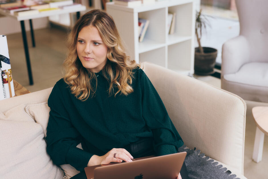 Na zdjęciu kobieta siedząca na jasnym fotelu, trzymająca laptop.