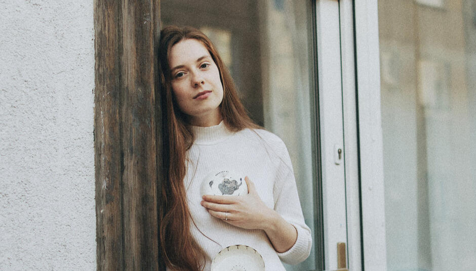Na zdjęciu kobieta o długich włosach, trzymająca ceramikę.