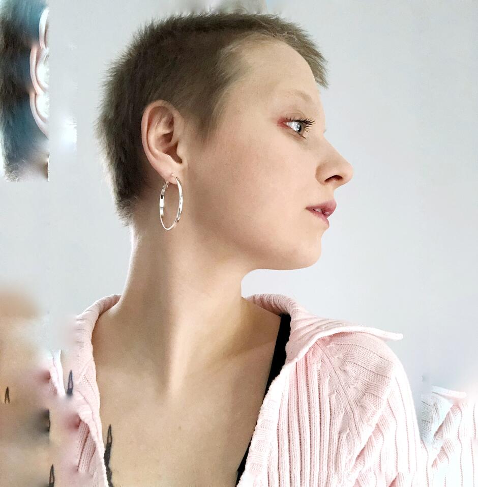 Na zdjęciu profil kobiety o krótkich włosach, z kolczykiem w kształcie okręgu w uchu.