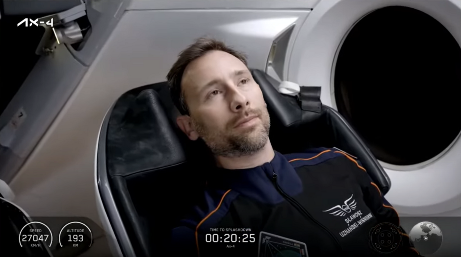 Na zdjęciu widać astronautę w skafandrze z nazwiskiem „Uznański - Wiśniewski” siedzącego w fotelu wewnątrz kapsuły kosmicznej. Na ekranie widnieją informacje o prędkości, wysokości oraz czasie pozostałym do wodowania statku misji Ax-4.