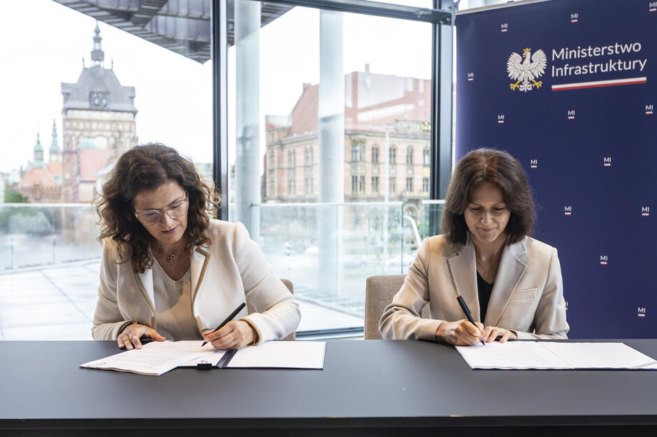 na zdjęciu dwie kobiety w średnim wieku, siedzą przy stole, podpisują dokumenty