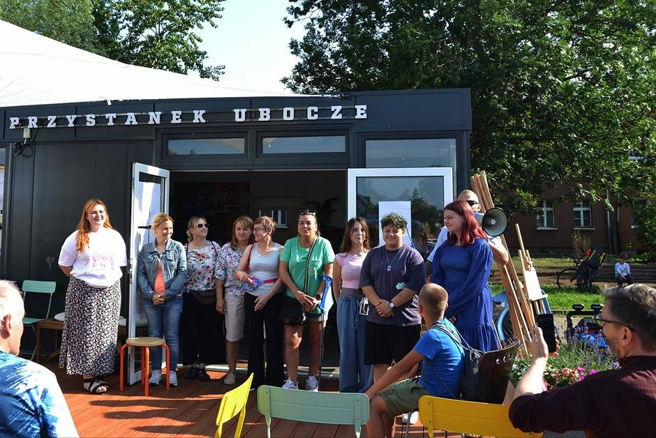 Członkowie oby rad stoją przed kontenerowym budynkiem z napisem Przystanek Ubocze