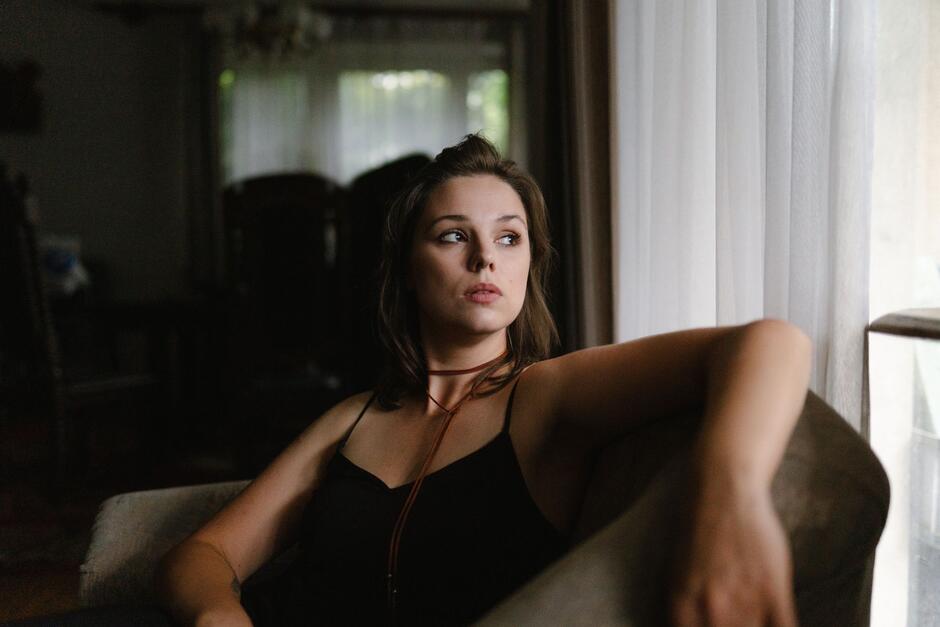 Na zdjęciu młoda kobieta w czarnej koszulce na ramiączkach, siedząca w fotelu.