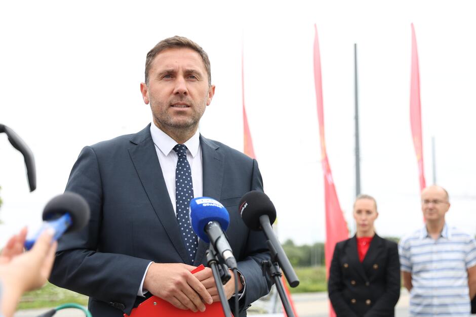 na zdjęciu mężczyzna w średnim wieku, w garniturze, mówi do dziennikarskich mikrofonów