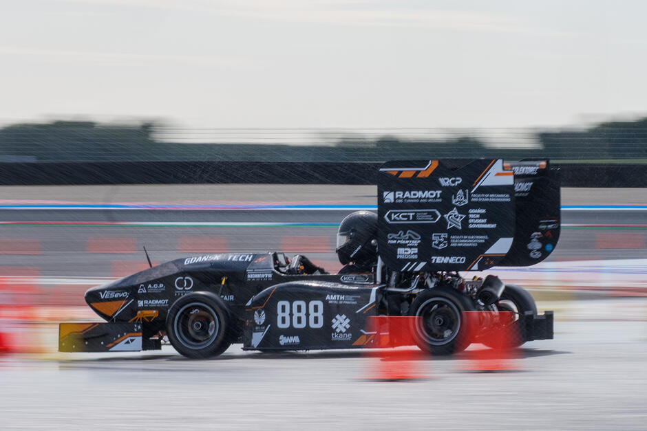 Bolid wyścigowy pędzi po torze, tło jest rozmyte, co daje efekt prędkości.