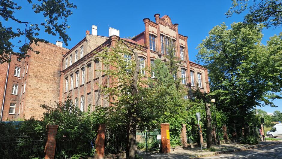 Duży ceglany budynek otoczony zielenią