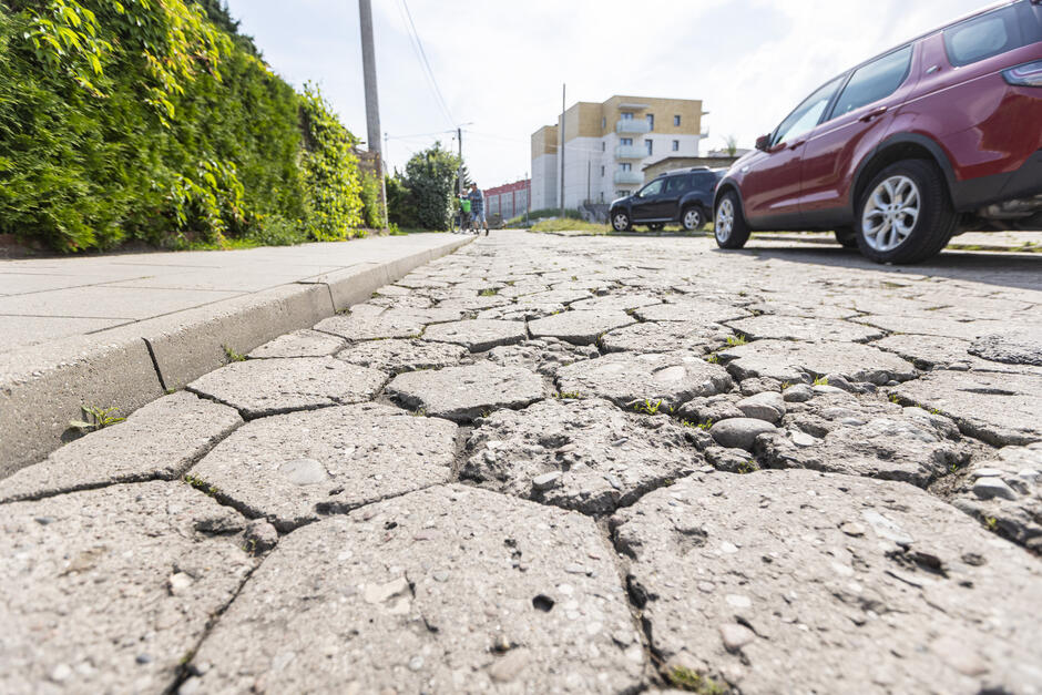 zbliżenie na zniszczoną jezdnię o nawierzchni z kostki typu trylinka, po prawej stoi samochód czerwony
