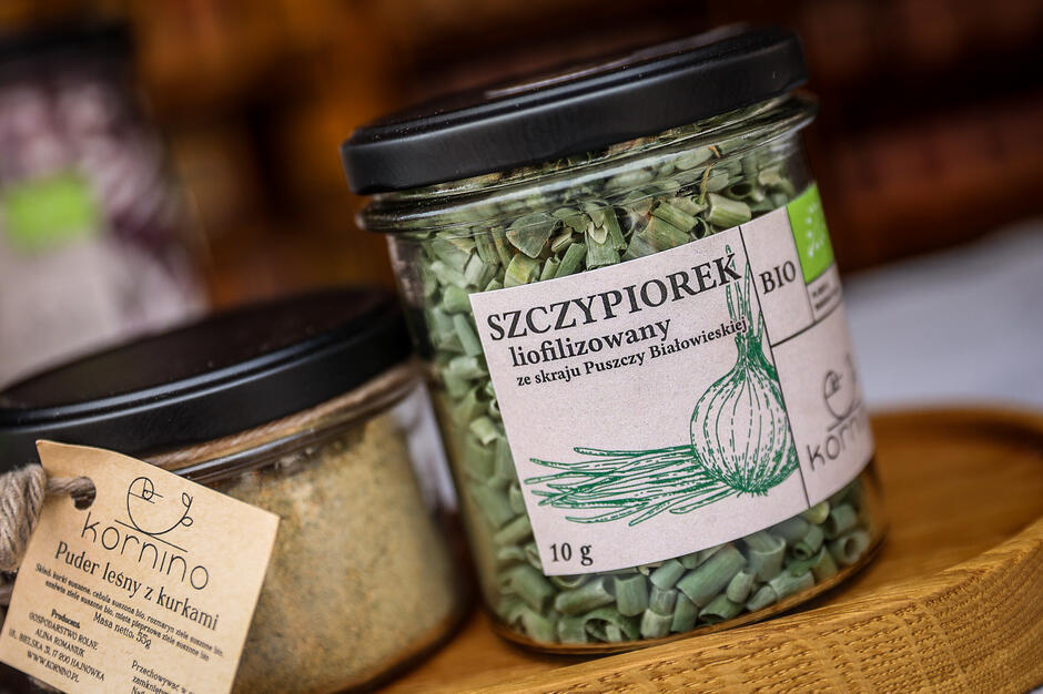 Na zdjęciu przedstawiono słoiczki z naturalnymi przyprawami marki Kornino – liofilizowanym szczypiorkiem oraz pudrem leśnym z kurkami. Produkty te pochodzą z ekologicznego gospodarstwa położonego na skraju Puszczy Białowieskiej i wyróżniają się estetycznym opakowaniem oraz regionalnym charakterem.
