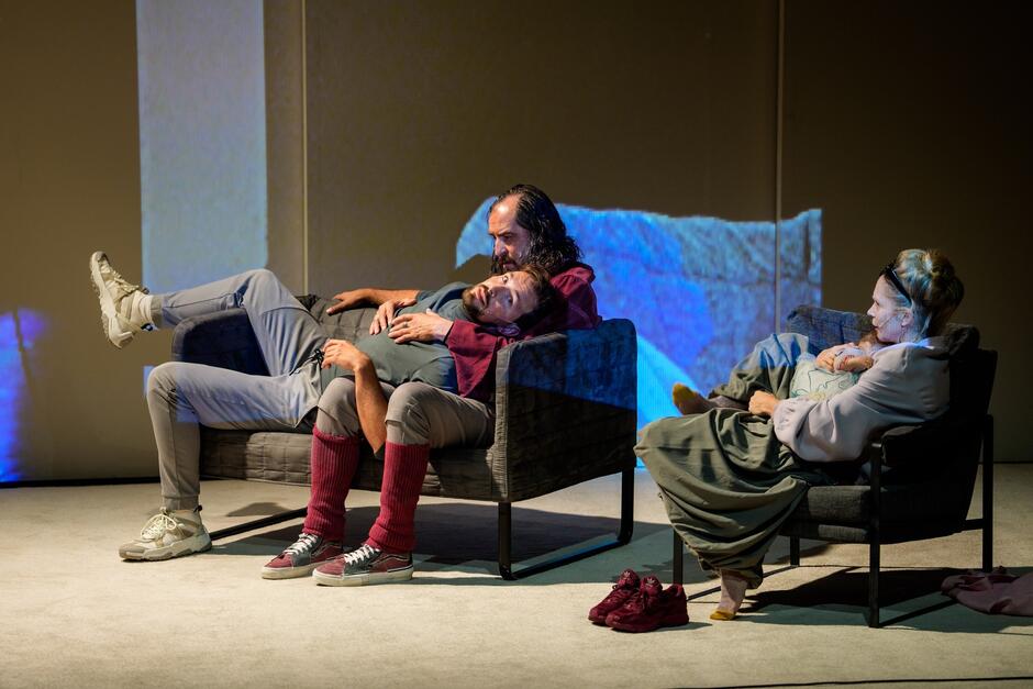 Po lewej kozetka z siedzącymi na niej dwoma aktorami, po prawej fotel, w którym siedzi aktorka