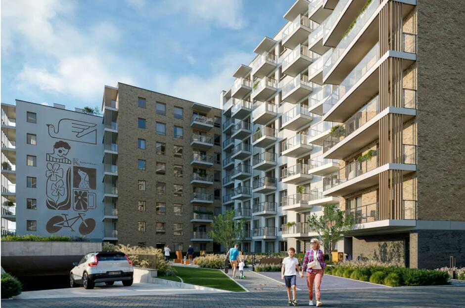 Nowoczesne osiedle mieszkaniowe prezentuje elegancką architekturę z przestronnymi balkonami oraz starannie zagospodarowaną przestrzenią wspólną z zielenią i miejscem do rekreacji. Na bocznej ścianie jednego z budynków znajduje się mural z symbolami codziennego życia, który nadaje całości artystyczny charakter.
