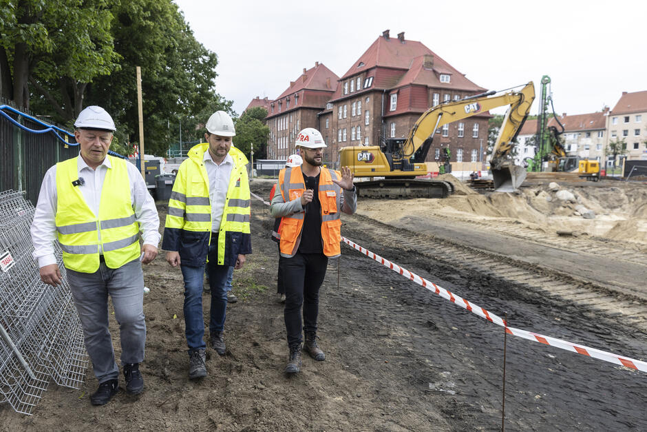trzech mężczyzn idzie po placu budowy, wokół rozkopany teren