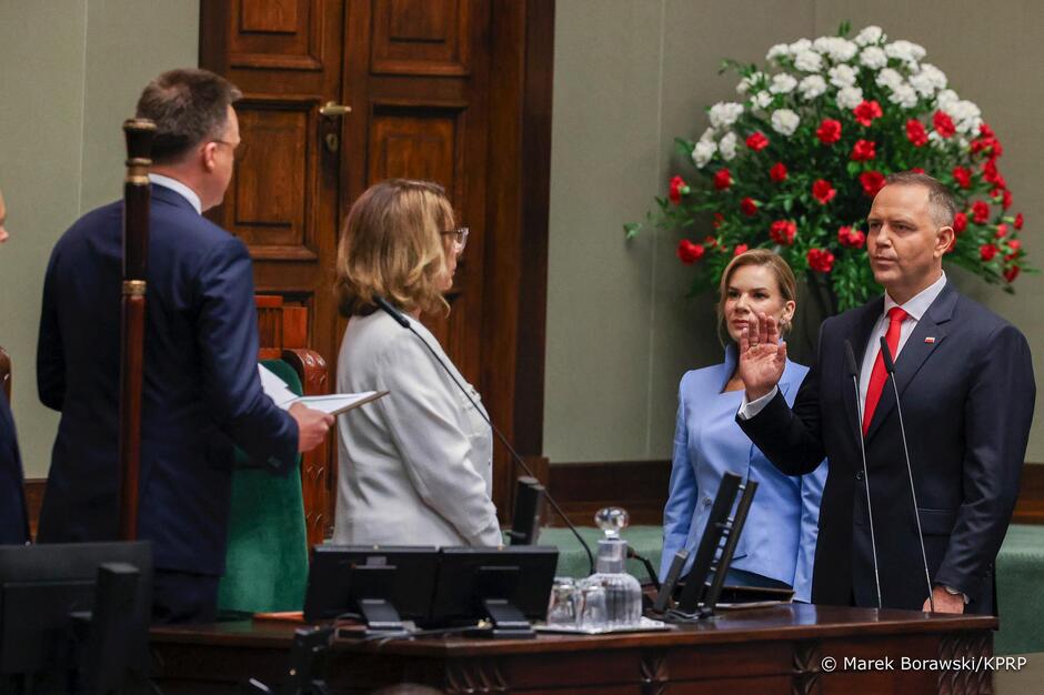 Cztery osoby na zdjęciu - Karol Nawrocki z ręką uniesioną do ślubowania