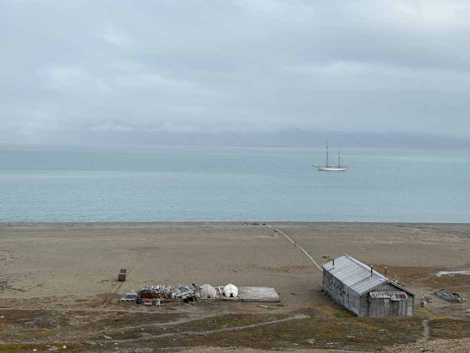 Na zdjęciu znajduje się Stacja Polarna Uniwersytetu Marii Curie-Skłodowskiej w Calypsobyen, położona w surowym, arktycznym krajobrazie. Budynek otaczają góry, śnieg i tundra, co podkreśla jego odizolowanie i naukowy charakter ekspedycji. 