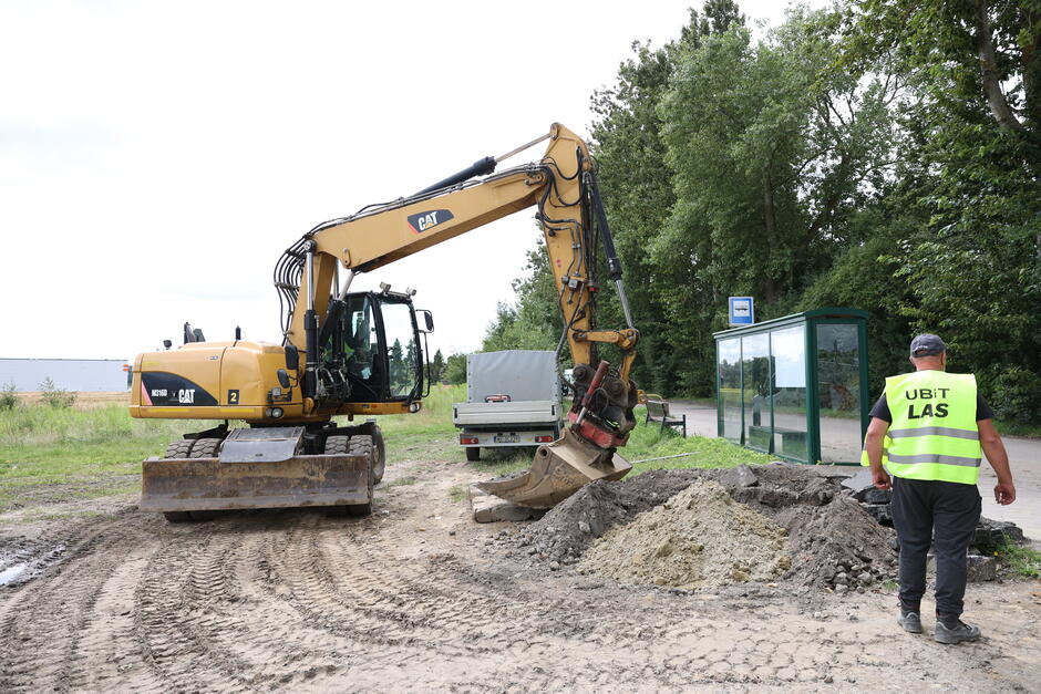 na zdjęciu z lewej żółta koparka, jest rozkopany grunt, po prawej stoi robotnik