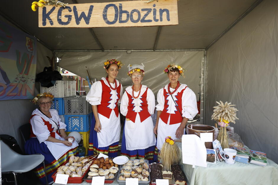 Stragan na festynie z lokalnymi wyrobami, na straganie kobiety ubrane w stroje ludowe.