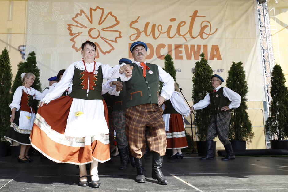 Kobieta i mężczyzna w strojach ludowych tańczą na scenie.