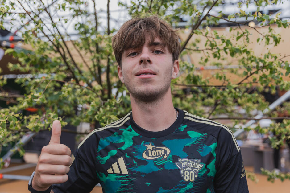 Młody mężczyzna pozuje do zdjęcia w zielonej koszulce Lechii