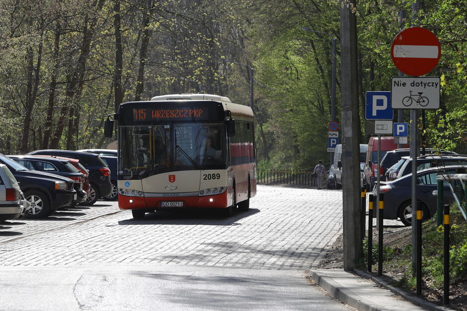 Na zdjęciu widać autobus komunikacji miejskiej marki Solaris o numerze taborowym 2089, jadący linią 115 w kierunku „Wrzeszcz PKP”. Autobus porusza się po ulicy wyłożonej kostką brukową, otoczoną z jednej strony zaparkowanymi samochodami, a z drugiej drzewami w wiosennej zieleni.