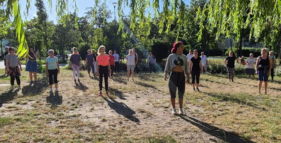 na zdjęciu kilkanaście kobiet w sportowych strojach ćwiczy w parku