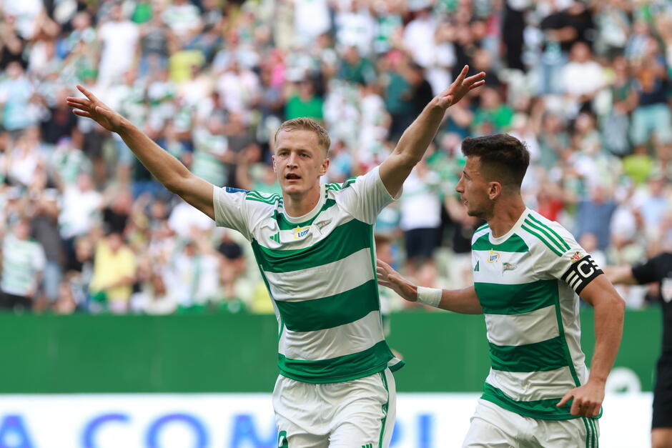 Dwaj zawodnicy w biało-zielonych strojach, cieszą się ze zdobycia bramki