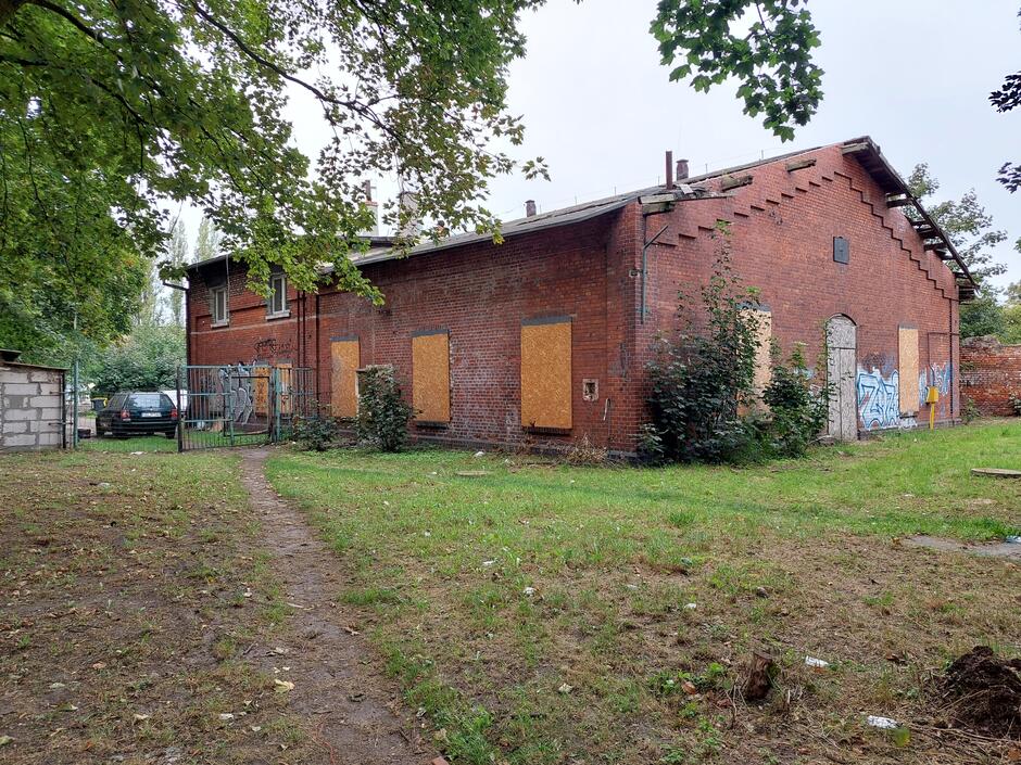 Stary parterowy budynek z cegły, z otworami okiennymi zabitymi płytami wiórowymi