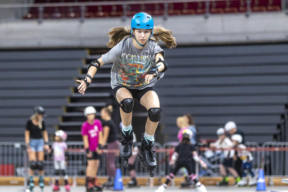 na zdjęciu dziewczyna skacząca przez przeszkodę, w rolkach i kasku na głowie