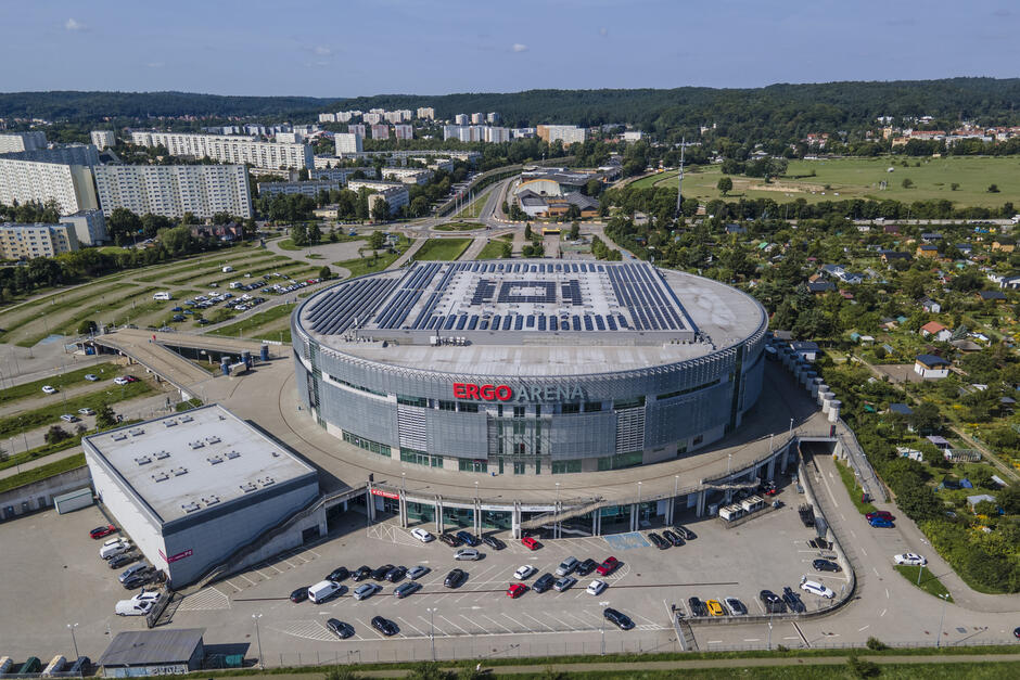 widok z drona na okrągłą halę widowiskową, w tle osiedle wysokich bloków mieszkalnych
