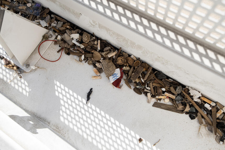 Wnętrze pojemnika robota sprzątającego plażę, w środku niedopałki papierosów, papierki, pestki, patyczki.