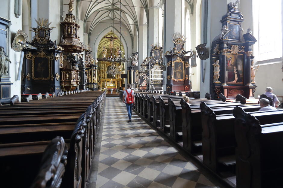 wnętrze kościoła, widać drewniane brązowe ławki dla wiernych, na kolumnach ogromne obrazy w bogatych ramach