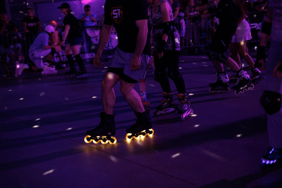 Grupa osób jadących na rolkach, jedne z rolek mają świecące kółka