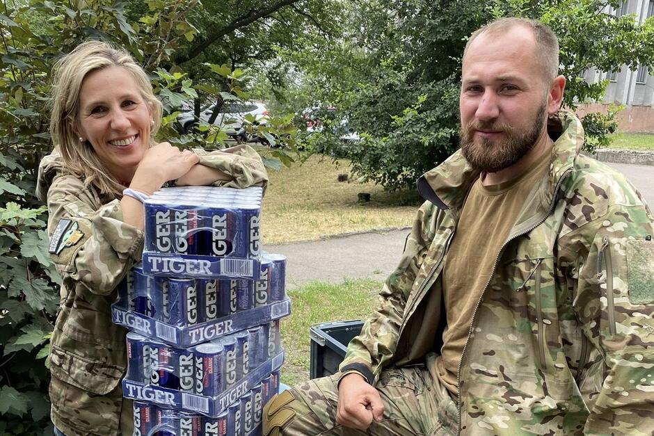 Dwie osoby w strojach moro, po lewej kobieta, po prawej - mężczyzna. Między nimi puszki z napojami energetyzującymi