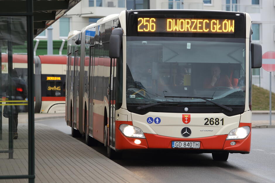 na zdjęciu autobus miejski w kolorach kremowo czerwonym, stoi przy wiacie przystankowej