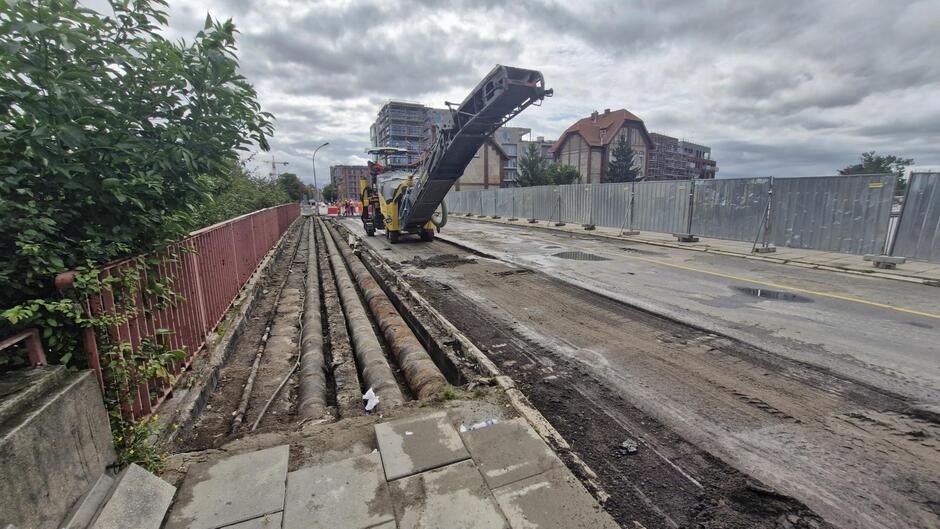 na zdjęciu koparka na moście, widać częściowo rozebrana nawierzchnię i odsłonięte rury po lewej stronie