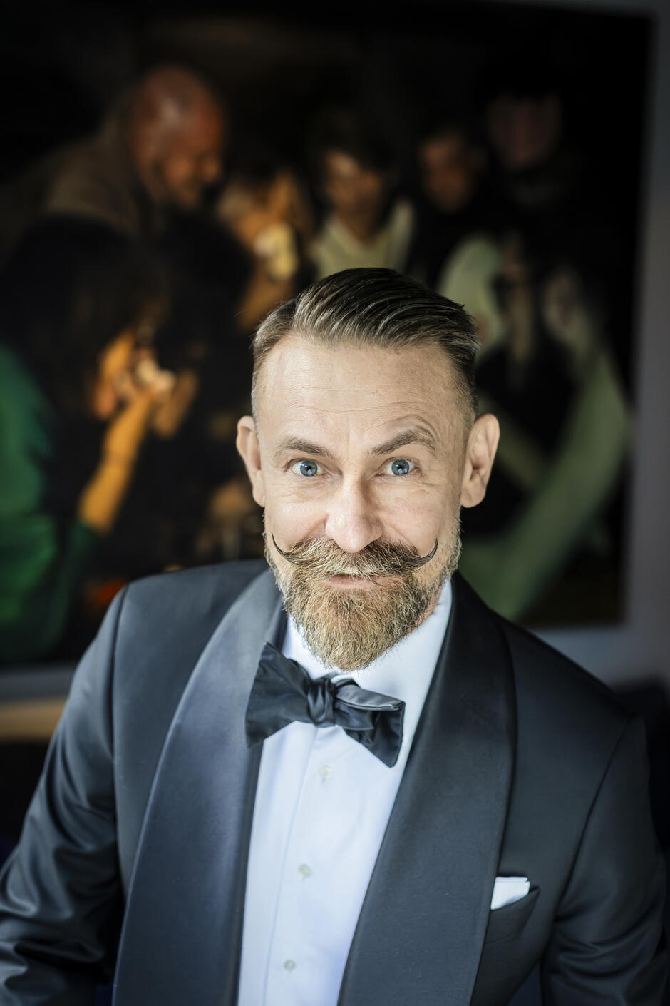 Na zdjęciu mężczyzna z wywiniętym wąsem i brodą, ubrany w garnitur.