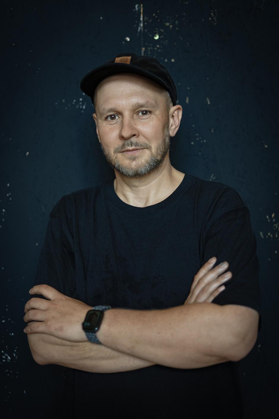 Na zdjęciu mężczyzna w czarnej koszulce, w czarnej czapce z daszkiem.