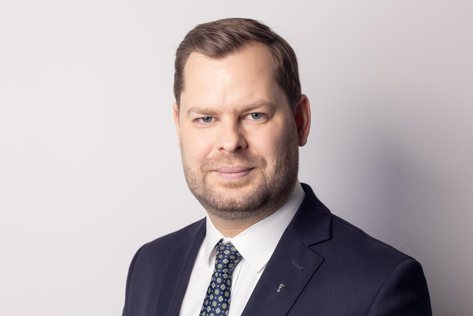 Na zdjęciu mężczyzna z lekkim zarostem, z krótkimi włosami, ubrany w garnitur.