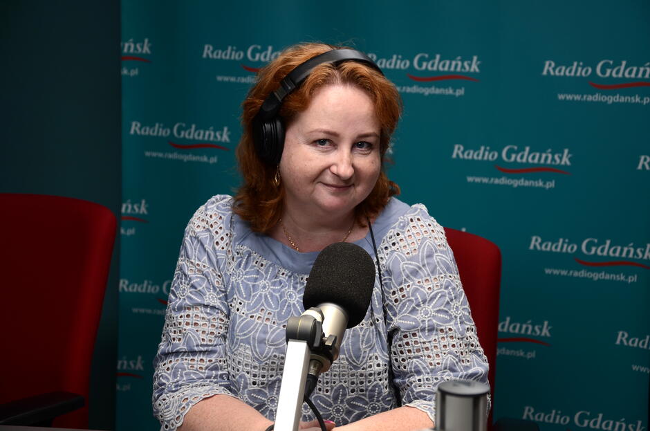 Na zdjęciu kobieta siedząca przed mikrofonem radiowym i słuchawkach na uszach.