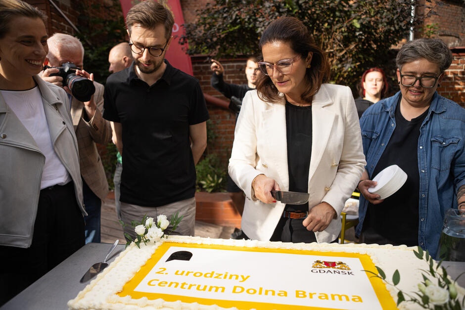 Cztery osoby nad tortem urodzinowym. Jedna kobieta z nożem do krojenia.