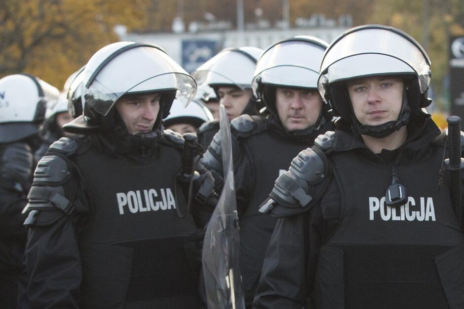 Policjanci w białych hełmach ochronnych, napierśnikach i z tarczami