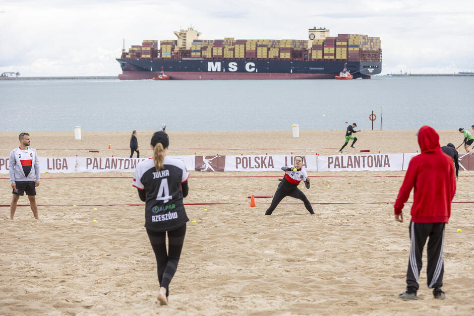 Zawodnicy grają na plaży - w tle duży statek na wodach Zatoki Gdańskiej