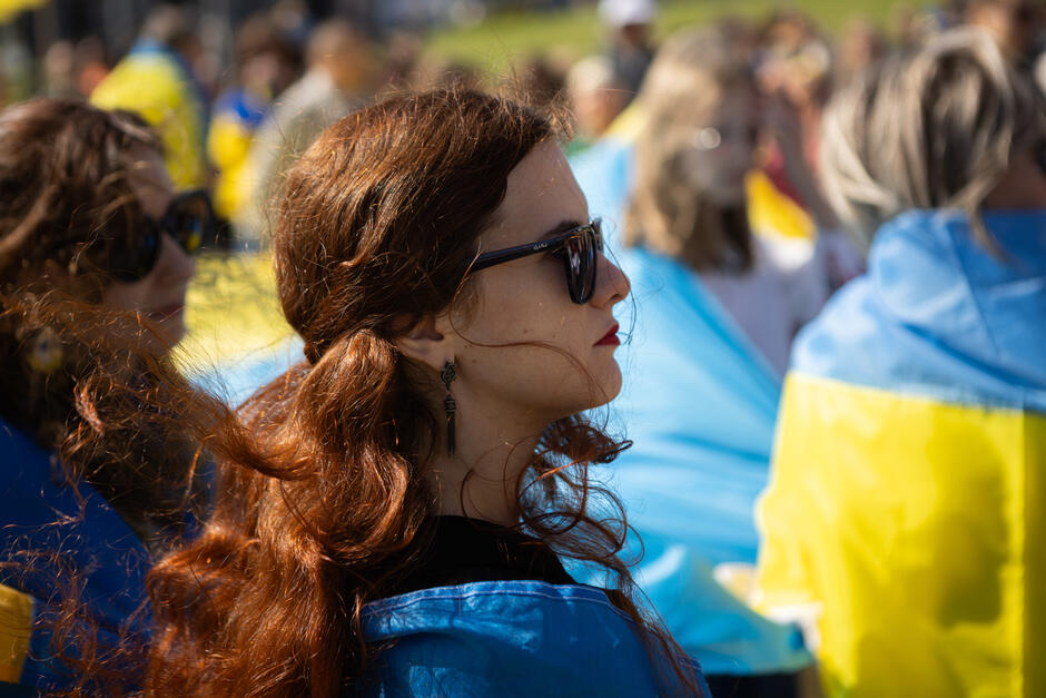 Profile kobiet uczestniczących w manifestacji, na tle niebiesko-żółtych flag Ukrainy