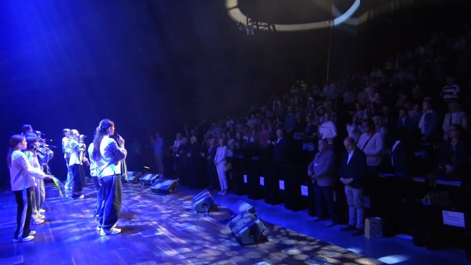 Po lewej grupa młodzieży śpiewającej na scenie - po prawej widownia