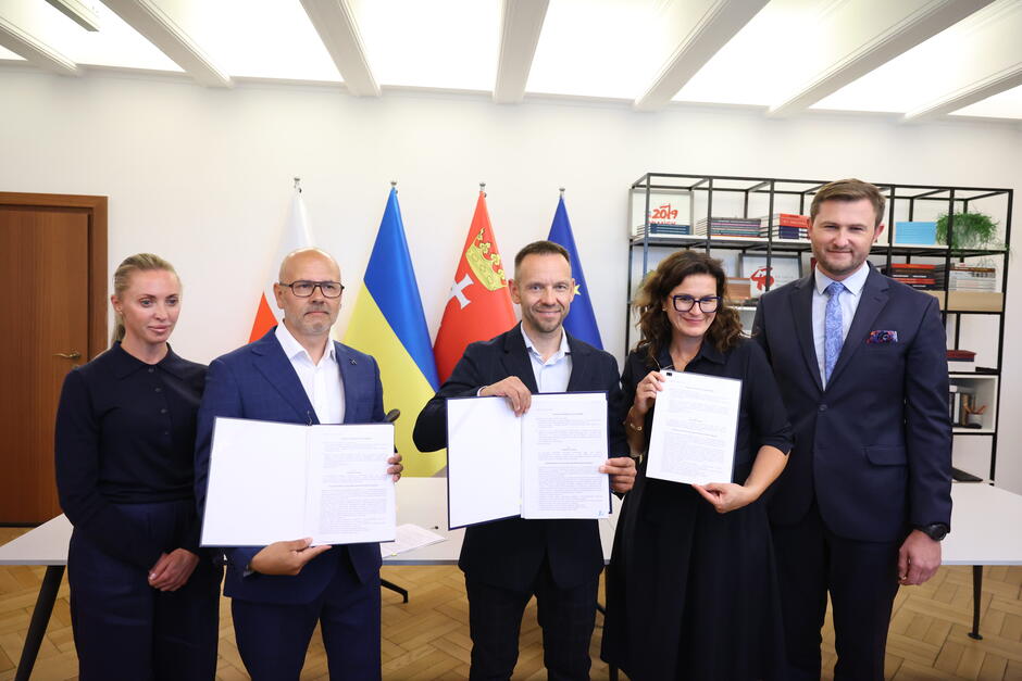 na zdjęciu dwie kobiety i trzech mężczyzn w średnim wieku, trzy osoby pozują z dokumentami w ręce