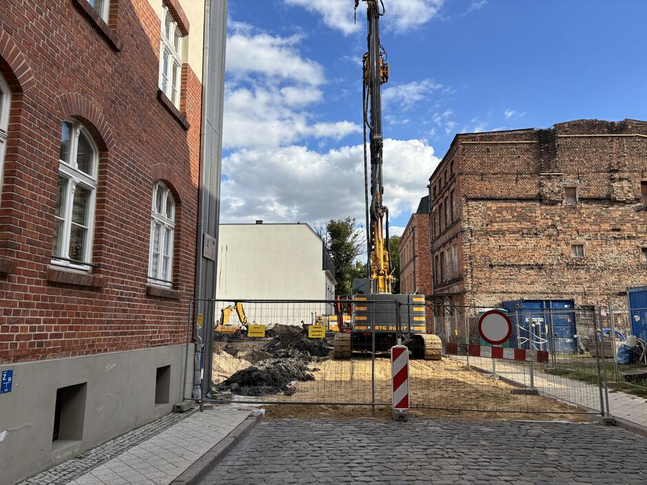 Ulica ogrodzona siatką, za nią wysoka maszyna - palownica