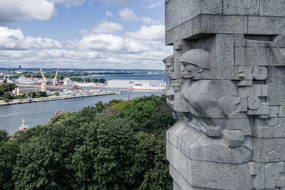 po prawej zbliżenie na fragment pomnika na westerplatte, w tle widok na port morski